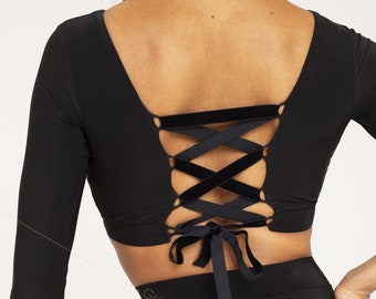 May include: Black long-sleeved crop top with a lace-up back detail. The top is made of a stretchy fabric and has a scoop neckline. The back features a criss-cross design with a velvet ribbon.