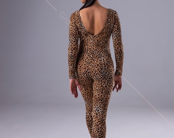 May include: A woman wearing a brown and black leopard print jumpsuit with long sleeves and a low back. She is wearing brown heeled shoes and has her hair pulled back in a ponytail.