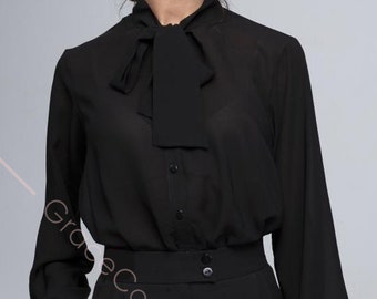 Może przedstawiać: Czarna bluzka z długim rękawem, z kokardką i zapięciem na guziki z przodu. Bluzka wykonana jest z przezroczystej tkaniny i ma dopasowany krój.