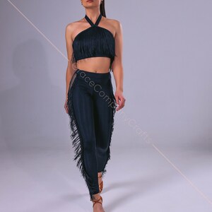 May include: A black halter top and matching pants with fringe trim. The top is a cropped style and the pants are fitted. The model is wearing brown sandals.