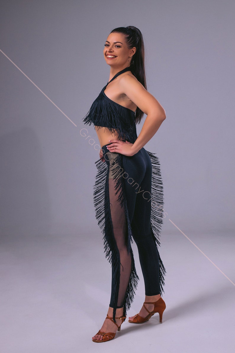 May include: A woman wearing a black fringe top and matching leggings with a sheer panel. She is wearing brown dance shoes and has her hair pulled back in a ponytail.
