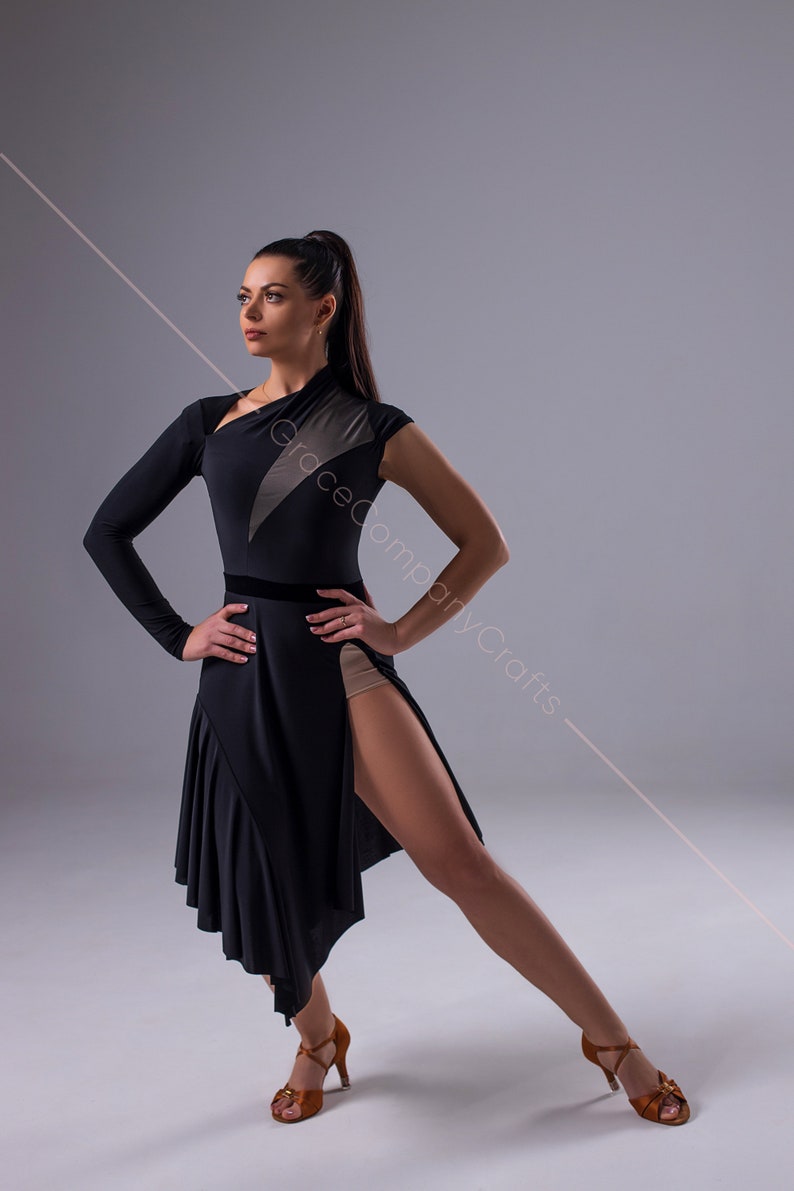 May include: A woman wearing a black dance dress with a sheer panel and a high slit. She is wearing brown dance shoes and has her hair pulled back in a ponytail.
