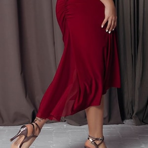May include: A woman wearing a long, burgundy dress with a lace-up back detail. She is wearing silver high-heeled sandals.