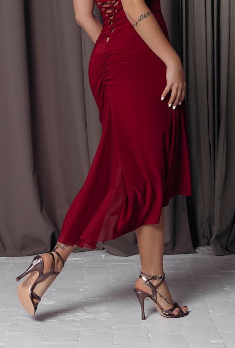 May include: A woman wearing a long, burgundy dress with a lace-up back detail. She is wearing silver high-heeled sandals.