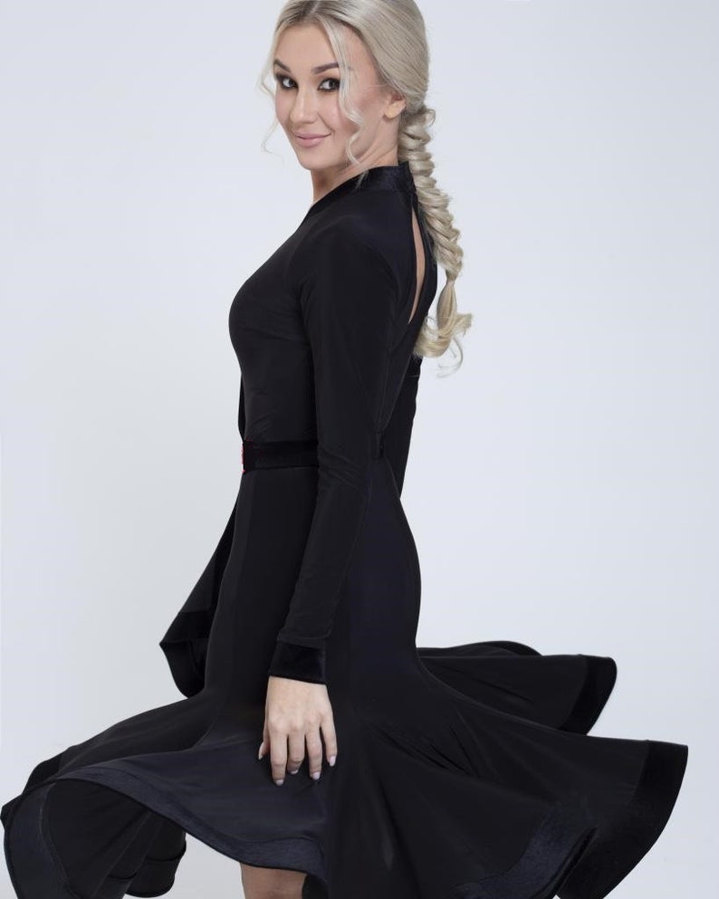 K&ouml;nnte beinhalten: Ein schwarzes Tanzkleid mit einem figurbetonten Oberteil und einem flie&szlig;enden Rock. Das Kleid hat einen hohen Ausschnitt und lange &Auml;rmel. Der Rock hat ein mehrschichtiges Design mit einem Samtbesatz.