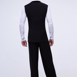 May include: A black sleeveless vest with a white long-sleeved shirt underneath. The person is wearing black pants and black shoes.