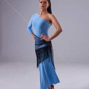 May include: A woman wearing a light blue one-shoulder dress with a black mesh shawl and fringe. She is wearing brown dance shoes and has her hair pulled back in a ponytail.