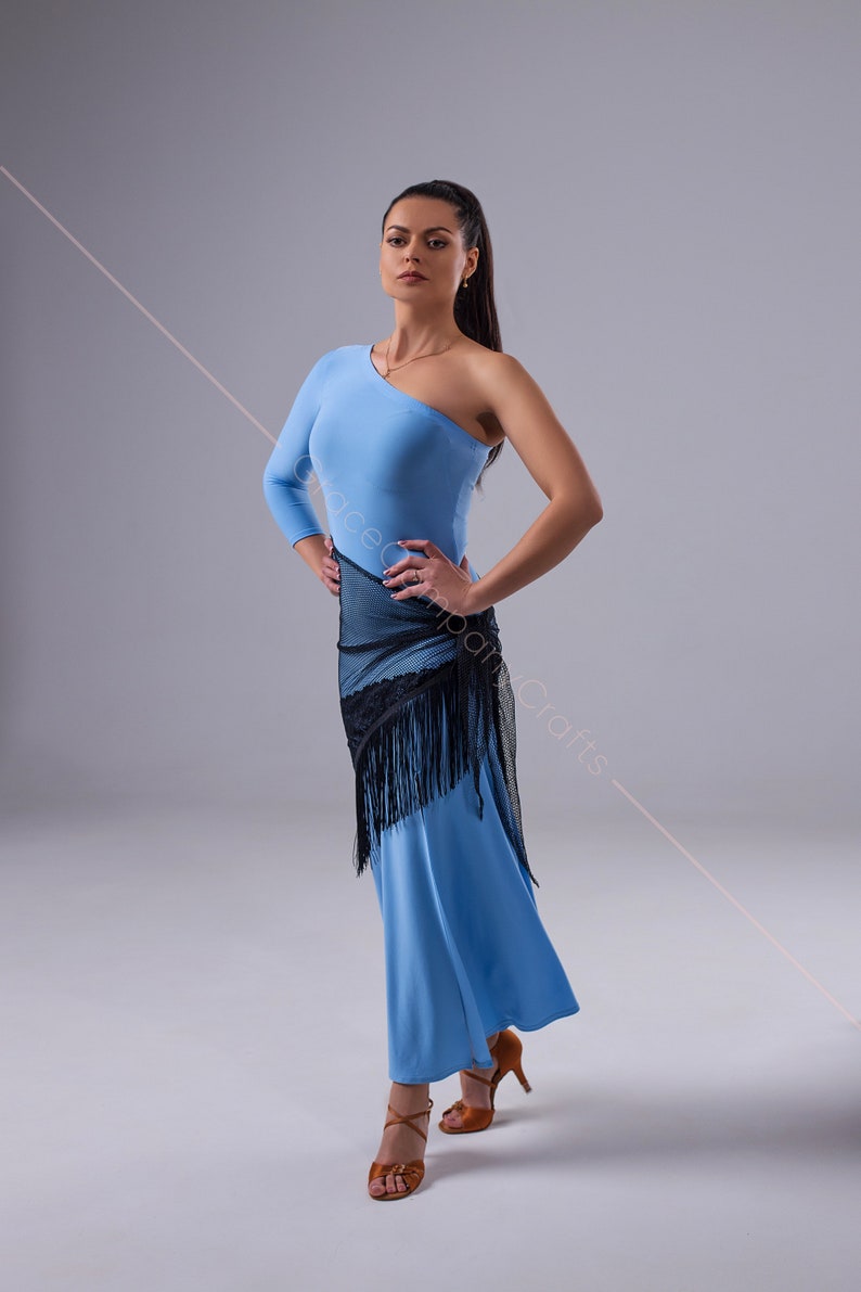 May include: A woman wearing a light blue one-shoulder dress with a black mesh shawl and fringe. She is wearing brown dance shoes and has her hair pulled back in a ponytail.