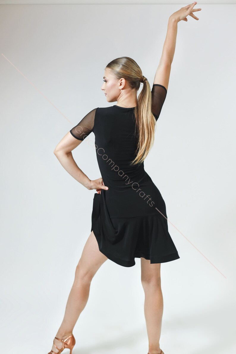 May include: A black dance dress with a mesh sleeve and a ruffled hem. The dress is fitted and has a scoop neckline.