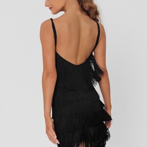 May include: A black mini dress with a fringe hem. The dress has a low back and spaghetti straps.