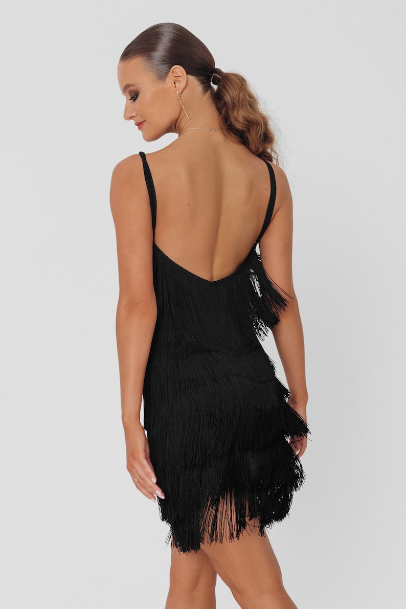 May include: A black mini dress with a fringe hem. The dress has a low back and spaghetti straps.