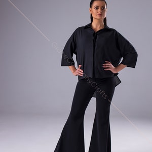 Puede incluir: Una mujer con una camisa negra de manga larga con cuello y cierre de botones. Tambi&eacute;n lleva pantalones negros acampanados y zapatos marrones.