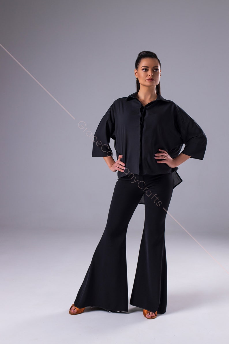 Puede incluir: Una mujer con una camisa negra de manga larga con cuello y cierre de botones. Tambi&eacute;n lleva pantalones negros acampanados y zapatos marrones.