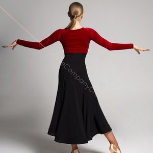 May include: A woman wearing a red velvet top and a black skirt. The skirt is long and flowing, and the top has long sleeves. The woman is standing with her arms outstretched, and her back is to the camera.