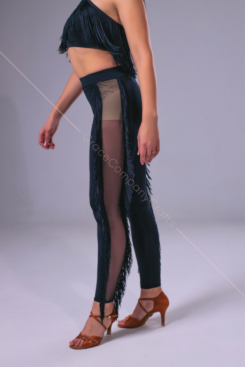 May include: Black dance leggings with fringe detail and a sheer panel on the side. The leggings are paired with brown dance shoes.
