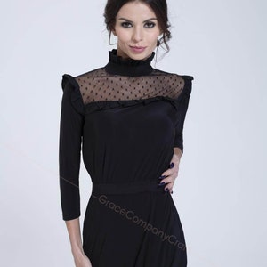 May include: A black mock neck dress with a sheer polka dot panel at the neckline. The dress has a ruffled neckline and a fitted bodice. The skirt is a-line and falls to the knees.
