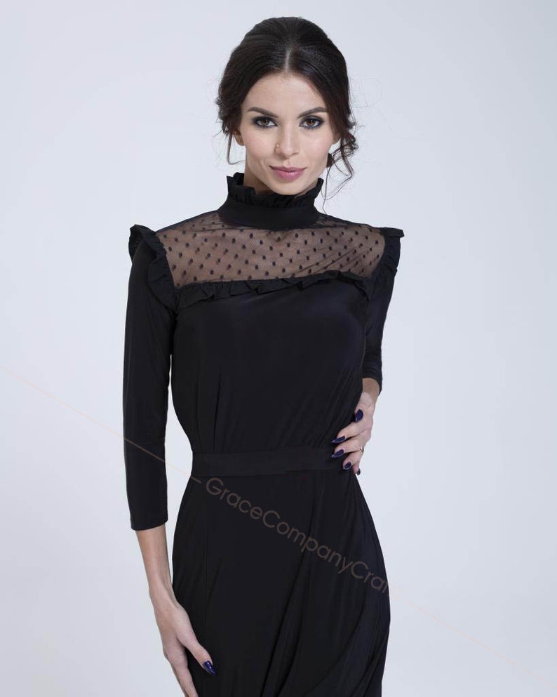 May include: A black mock neck dress with a sheer polka dot panel at the neckline. The dress has a ruffled neckline and a fitted bodice. The skirt is a-line and falls to the knees.