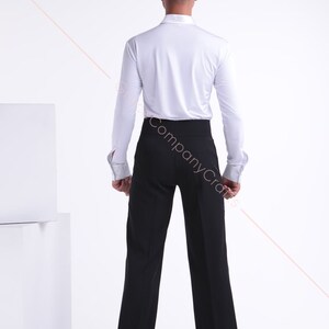 May include: A white long-sleeved shirt with a black pair of dress trousers. The shirt has a button-up collar and the trousers have a waistband.
