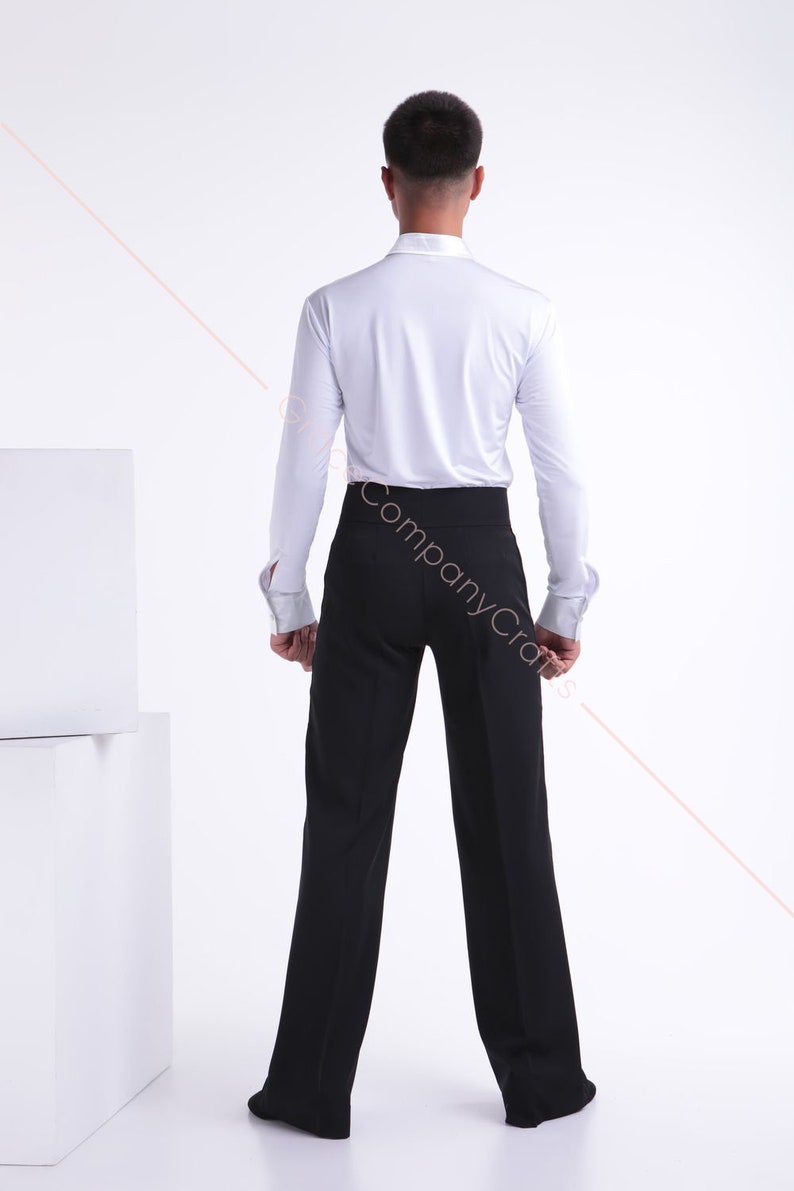 May include: A white long-sleeved shirt with a black pair of dress trousers. The shirt has a button-up collar and the trousers have a waistband.