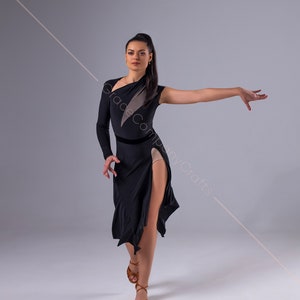 May include: A woman in a black dance dress with a side slit and a sheer panel on the left side. She is wearing brown dance shoes and has her hair pulled back in a ponytail.
