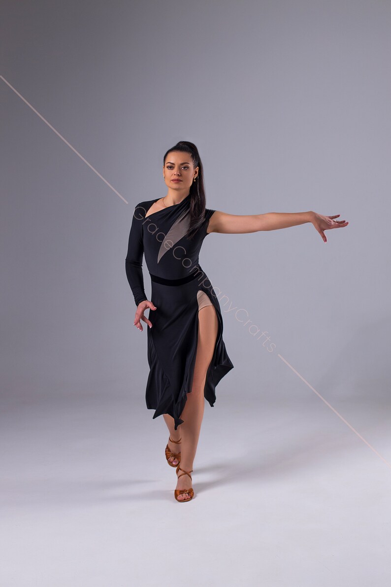 May include: A woman in a black dance dress with a side slit and a sheer panel on the left side. She is wearing brown dance shoes and has her hair pulled back in a ponytail.