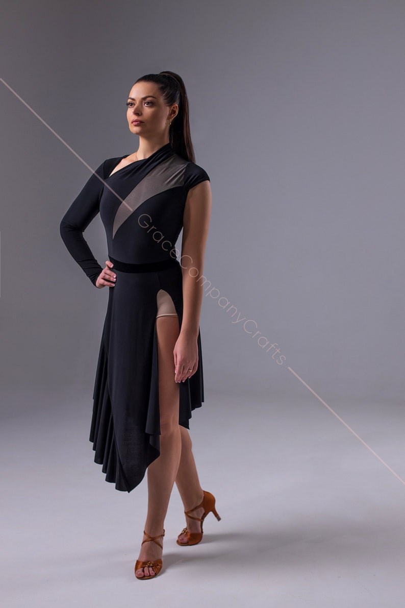May include: A woman wearing a black dance dress with a sheer panel and a high slit. The dress has a fitted bodice and a flowing skirt. She is wearing brown dance shoes.