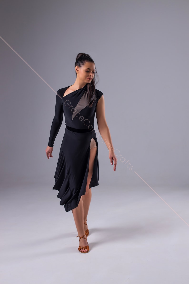 May include: A woman wearing a black dance dress with a sheer panel and a velvet waistband. She is wearing brown dance shoes and has her hair pulled back in a ponytail.