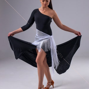 May include: A woman wearing a black one-shoulder dress with a white fringed shawl and brown dance shoes. She is posing with her arms outstretched and the skirt of her dress flowing behind her.