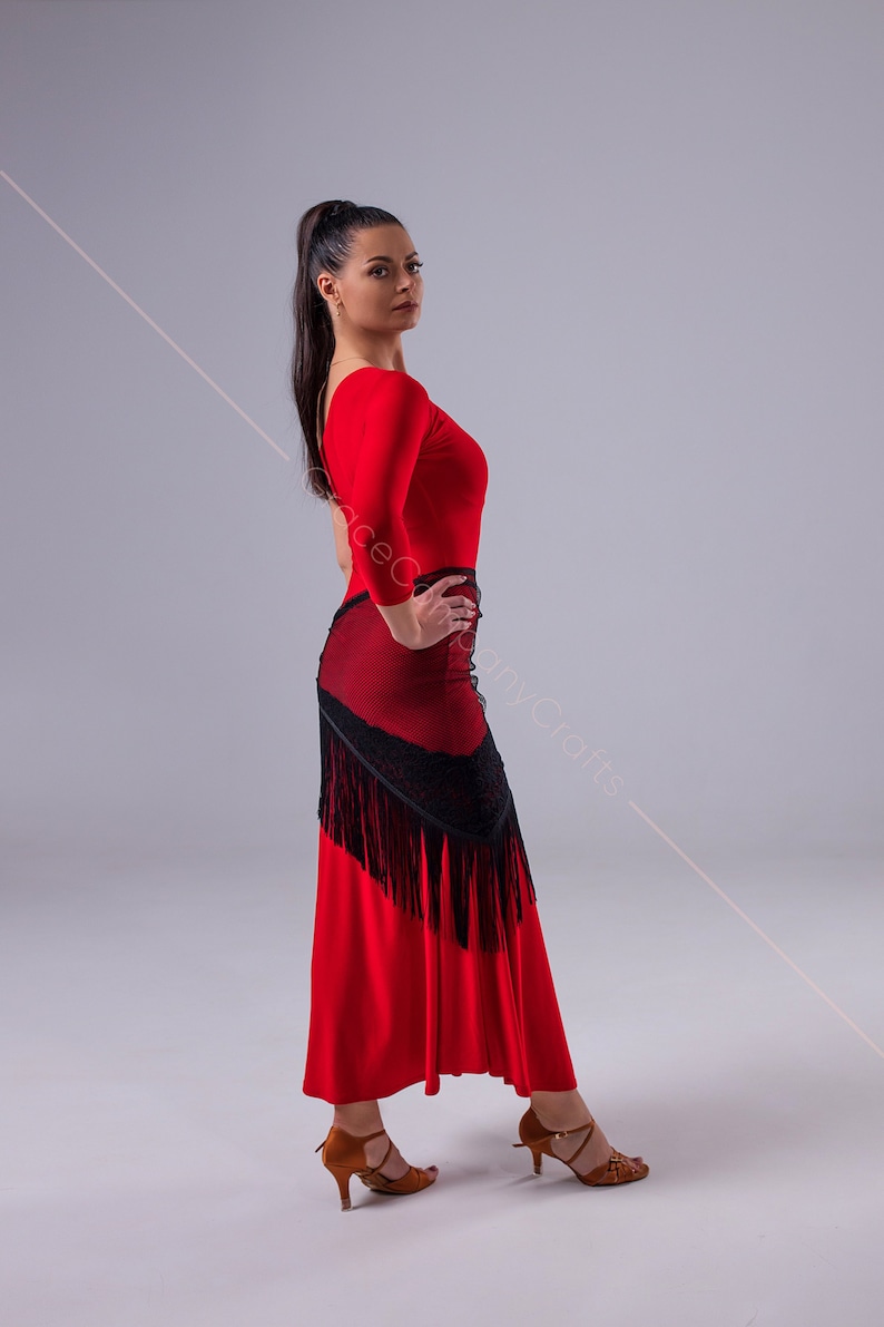 May include: A woman wearing a red long-sleeved top with a black lace and fringe skirt. She is wearing brown heeled shoes and has her hair pulled back in a ponytail.