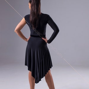 May include: A black dance dress with a long sleeve on one side and a short sleeve on the other. The dress has a black velvet waistband and a ruffled hem. The dress is asymmetrical, with the hem being longer on one side than the other.
