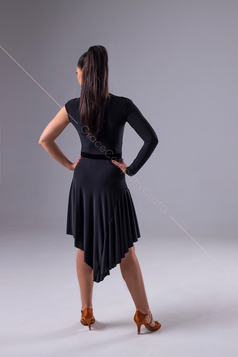 May include: A black dance dress with a long sleeve on one side and a short sleeve on the other. The dress has a black velvet waistband and a ruffled hem. The dress is asymmetrical, with the hem being longer on one side than the other.