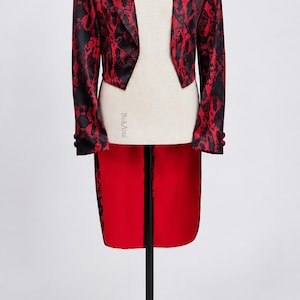 May include: A tailcoat jacket featuring a bold red and black snakeskin pattern. The garment has long sleeves with buttoned cuffs, a cropped front hem, and a long, solid red back panel. The interior lining of the back tails is a vibrant red fabric.