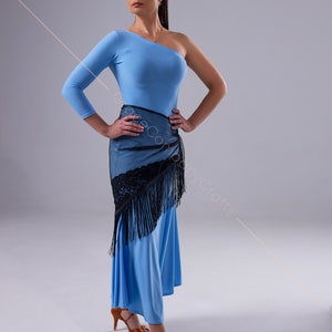 May include: A woman wearing a light blue one-shoulder dress with a black lace shawl and black fringe. She is wearing brown heeled sandals and has her hair pulled back in a ponytail.
