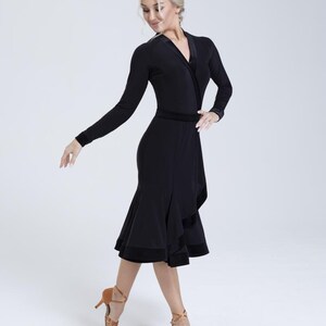 K&ouml;nnte beinhalten: Ein schwarzes Tanzkleid mit langen &Auml;rmeln, einem Wickel-Oberteil und einem gerafften Rock. Das Kleid hat einen Samtbesatz.