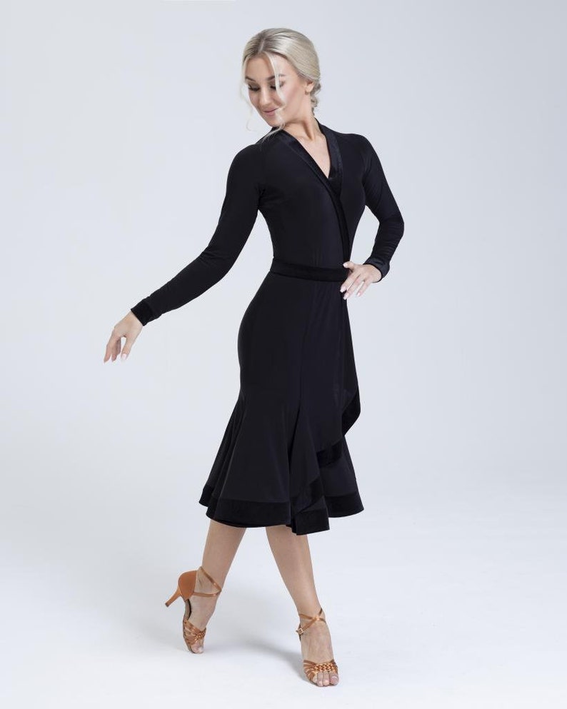 K&ouml;nnte beinhalten: Ein schwarzes Tanzkleid mit langen &Auml;rmeln, einem Wickel-Oberteil und einem gerafften Rock. Das Kleid hat einen Samtbesatz.