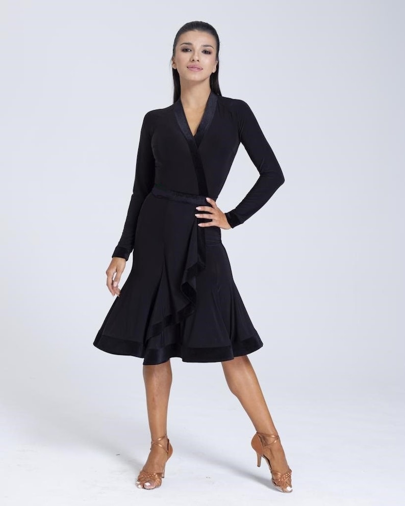 K&ouml;nnte beinhalten: Ein schwarzes Tanzkleid mit langen &Auml;rmeln, einem Wickel-Oberteil und einem gerafften Rock. Das Kleid hat einen Samtbesatz und eine Satinschleife.