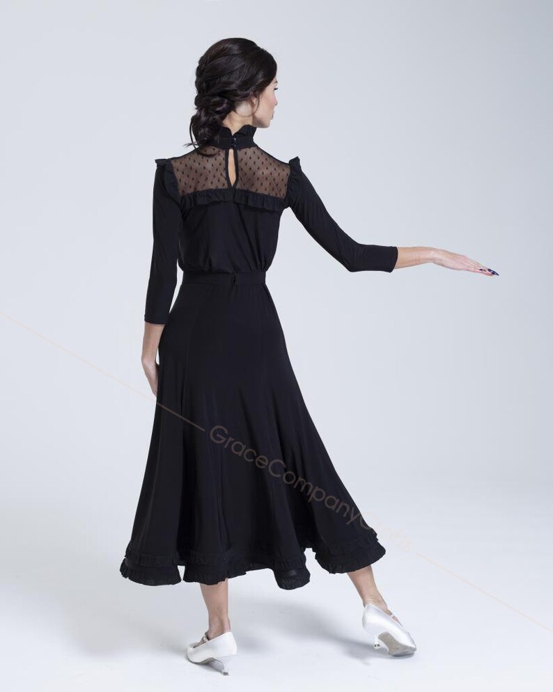 May include: A black dance skirt with a ruffled hem and a black long-sleeved top with a sheer lace yoke. The top has a high neck and a keyhole opening at the back.