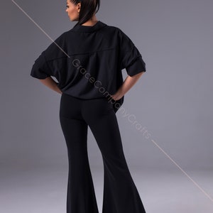 Puede incluir: Una camisa negra de manga corta con cuello y corte holgado y pantalones negros acampanados. La camisa tiene un cierre de bot&oacute;n &uacute;nico en el cuello.