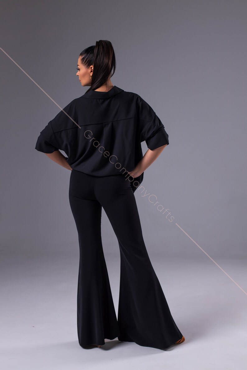 Puede incluir: Una camisa negra de manga corta con cuello y corte holgado y pantalones negros acampanados. La camisa tiene un cierre de bot&oacute;n &uacute;nico en el cuello.