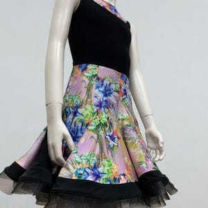 May include: A sleeveless dress with a black bodice and a floral print skirt. The skirt has a light purple background with blue, green, and white flowers. The hemline is trimmed with black fabric and a layer of black tulle.