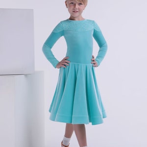 May include: A young girl wearing a turquoise velvet dress with a lace neckline. She is standing on a white background and has her hands on her hips.
