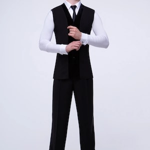 May include: A black vest with a velvet trim and a white dress shirt with a black tie. The man is wearing black pants and black shoes.