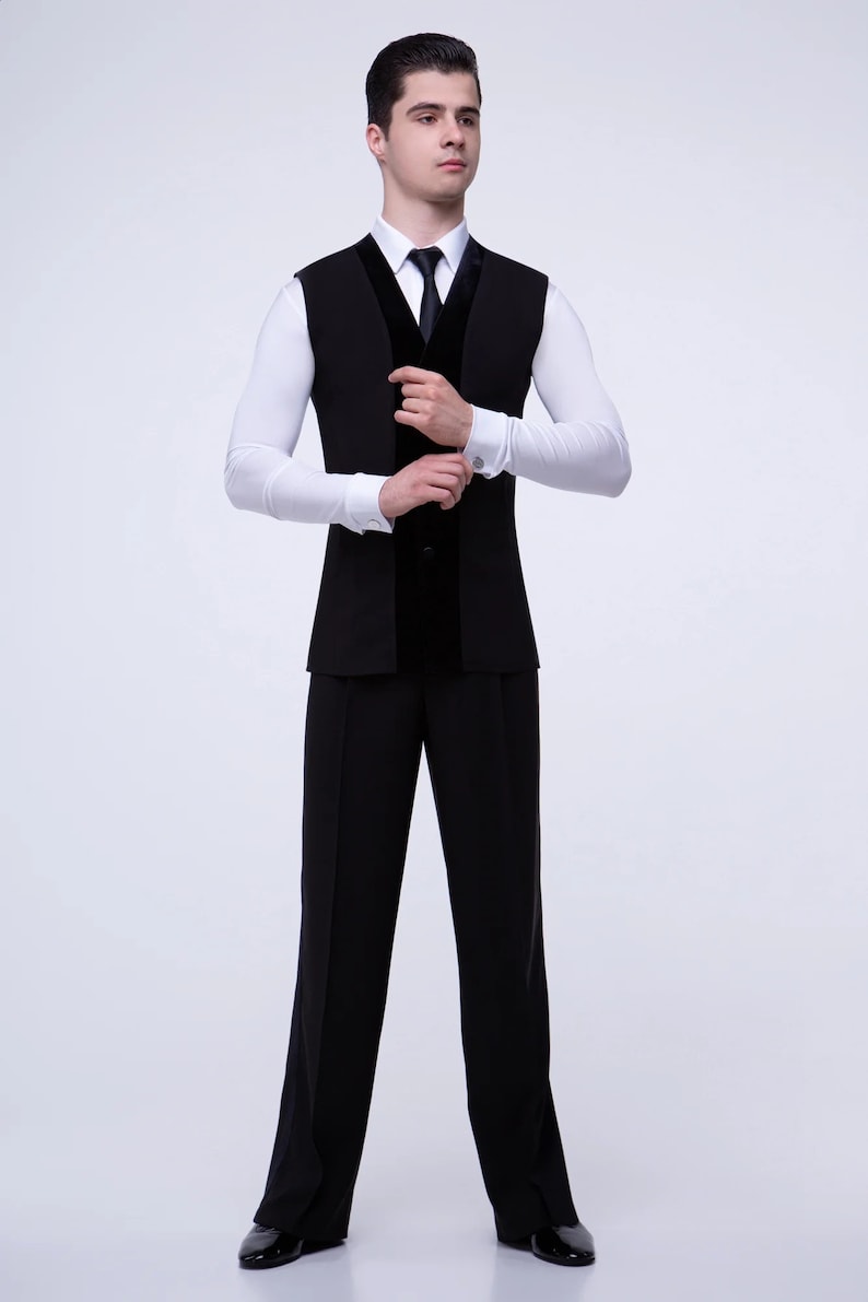 May include: A black vest with a velvet trim and a white dress shirt with a black tie. The man is wearing black pants and black shoes.