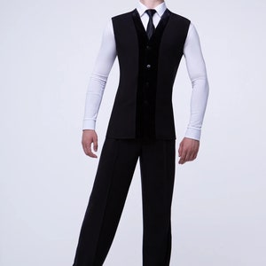 May include: A black sleeveless vest with a velvet panel down the front, worn over a white long-sleeved shirt with a black tie. The person is wearing black pants and black shoes.