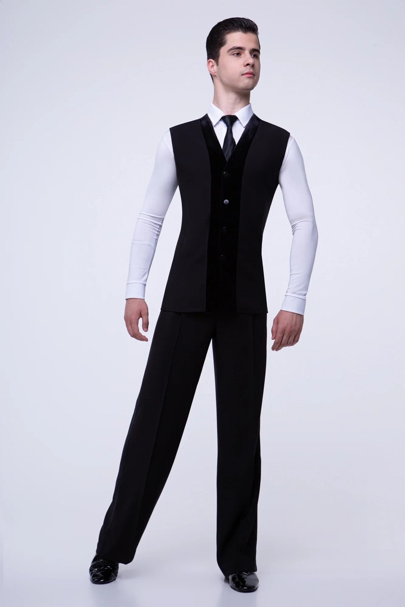 May include: A black sleeveless vest with a velvet panel down the front, worn over a white long-sleeved shirt with a black tie. The person is wearing black pants and black shoes.
