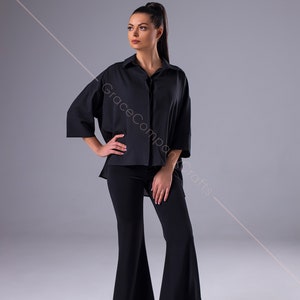 Puede incluir: Una mujer con una camisa negra de manga larga con cuello y pantalones negros acampanados. Est&aacute; de pie sobre un fondo gris.