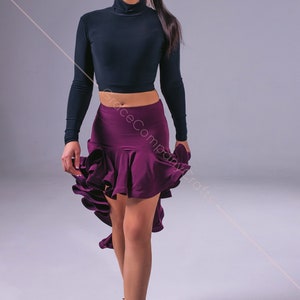 May include: A woman wearing a black long-sleeved crop top and a purple ruffled skirt. She is wearing brown dance shoes and has her hair pulled back in a ponytail.