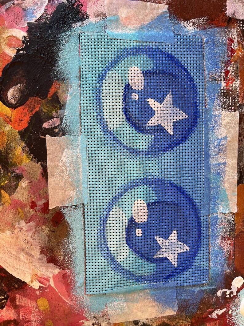 May include: A blue and white stencil with two circles containing a star and a bubble. The stencil is on a blue mesh background.