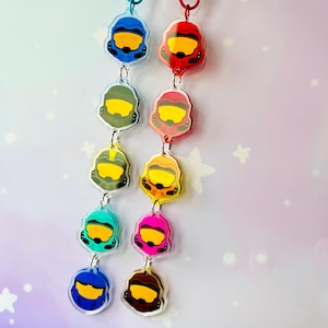 May include: Two vertical acrylic keyring strands featuring five helmet charms each. The left strand includes blue, olive, yellow, teal, and dark blue helmets. The right strand features red, pink, orange, magenta, and brown helmets, all with yellow visors.