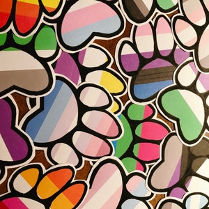 May include: A collection of paw print stickers with various pride flag colors, including rainbow, transgender, bisexual, and genderqueer.